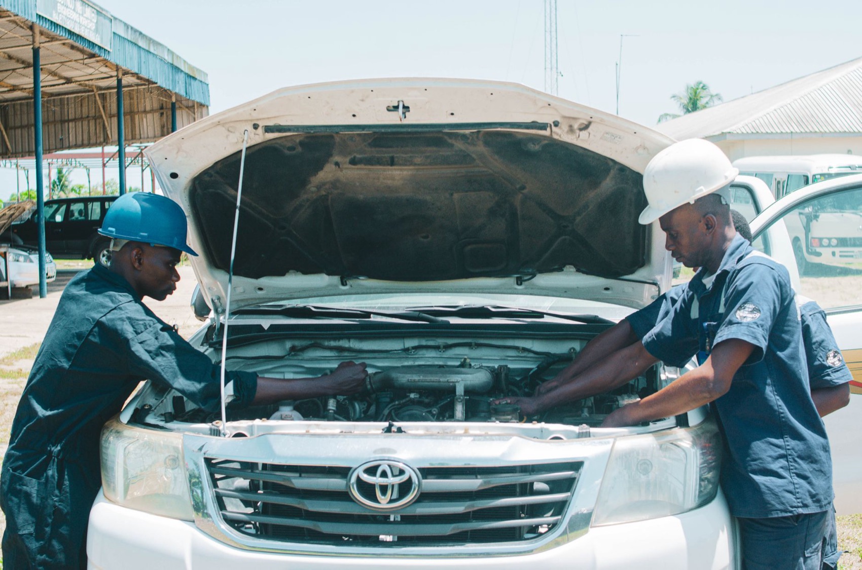 Two mechanics working under the bonnet of a white car.